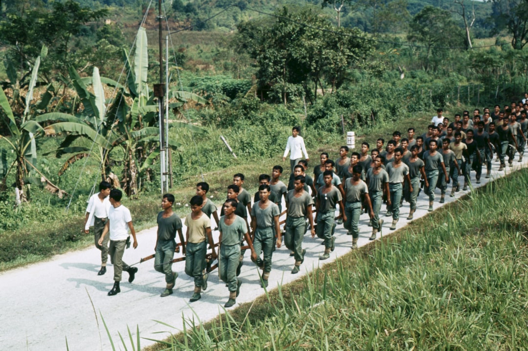 Soldiers marching down a rural road with lush vegetation.