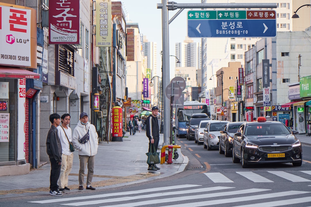 People wait at a crosswalk on a busy city street.