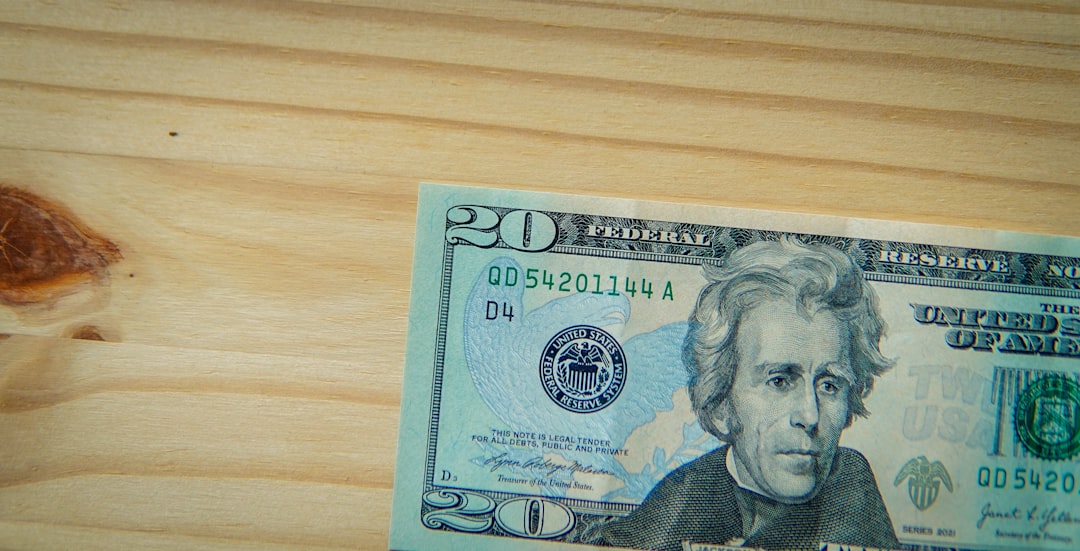 A twenty-dollar bill rests on a light wooden surface.