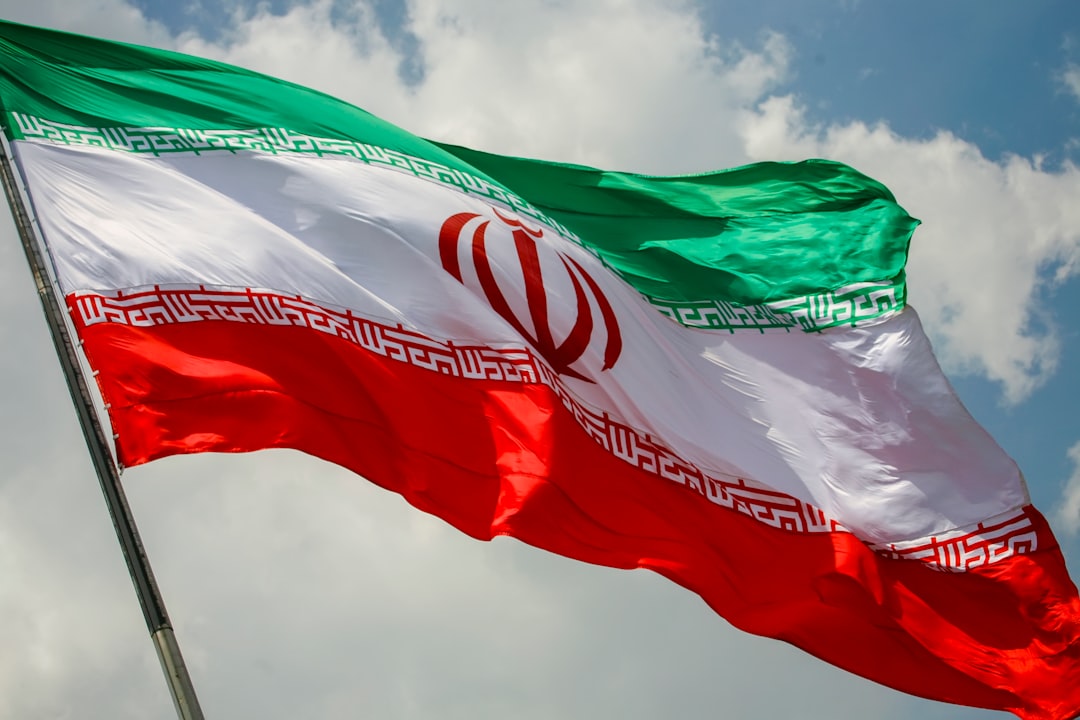 The flag of Iran waving against a blue sky with white clouds