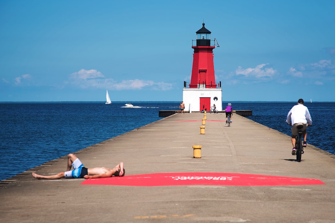 man in blue shorts lying on red concrete floor near white and red lighthouse during daytime
