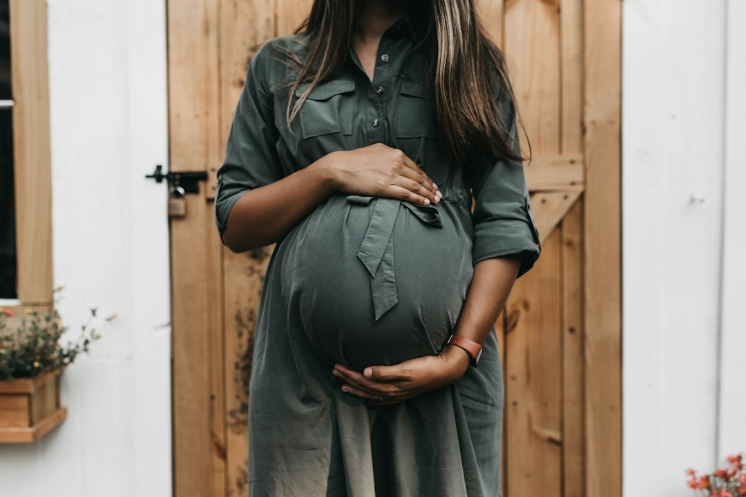 A pregnant woman in a green dress holding her belly before a wooden door