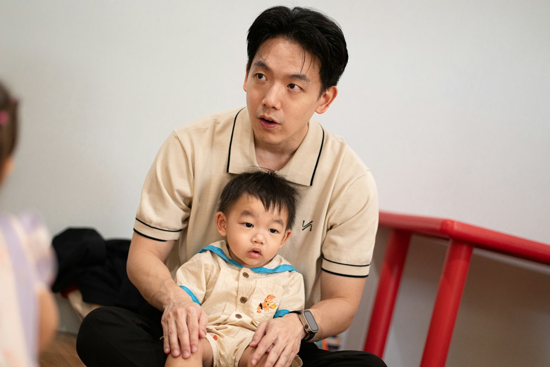 An adult holding a baby on his lap in a bright room
